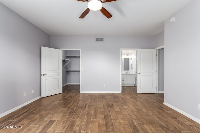 unfurnished bedroom with connected bathroom, ceiling fan, a closet, dark wood-type flooring, and a walk in closet