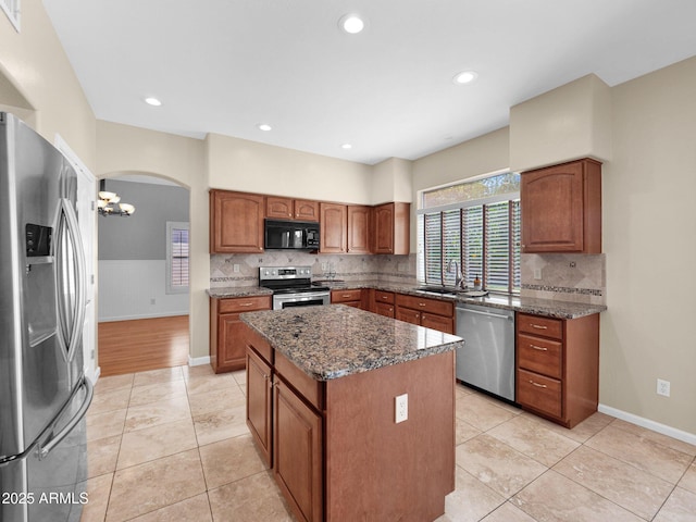 981 N Quail Ln, Gilbert, AZ 85233 - kitchen with appliances with stainless steel finishes, arched walkways, dark stone counters, brown cabinets, and a center island