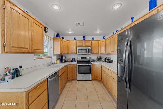 kitchen with sink, light tile patterned floors, light brown cabinets, and appliances with stainless steel finishes