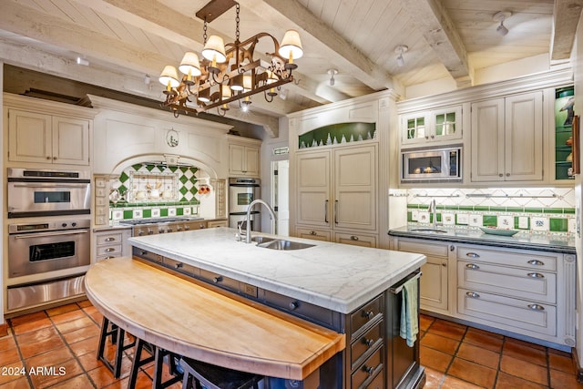 kitchen with cream cabinetry, pendant lighting, wooden ceiling, beamed ceiling, and an island with sink