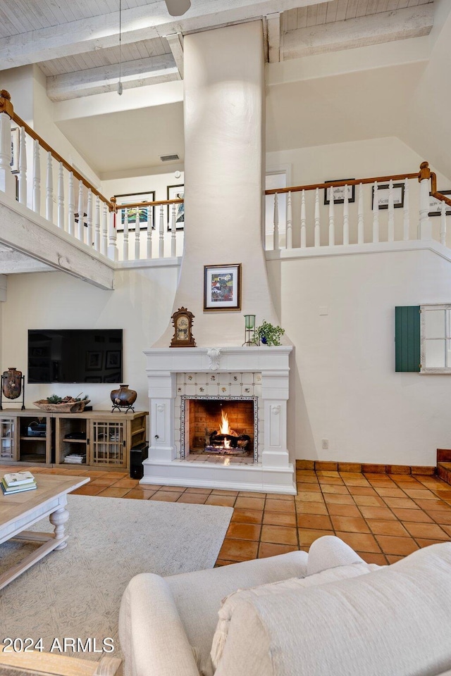 living room featuring beam ceiling, a tile fireplace, wooden ceiling, a high ceiling, and tile patterned floors