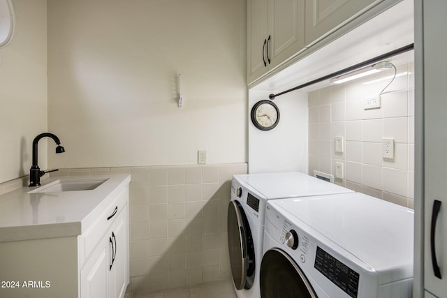 clothes washing area featuring sink, cabinets, tile walls, and independent washer and dryer