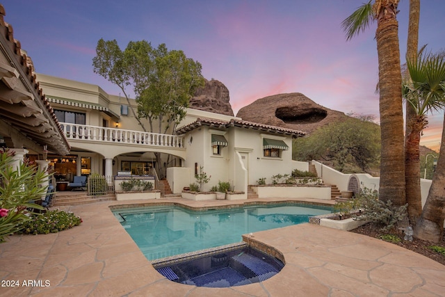 back house at dusk with a swimming pool with hot tub, a balcony, and a patio area