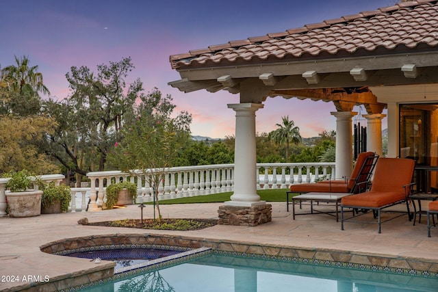 pool at dusk featuring an in ground hot tub and a patio