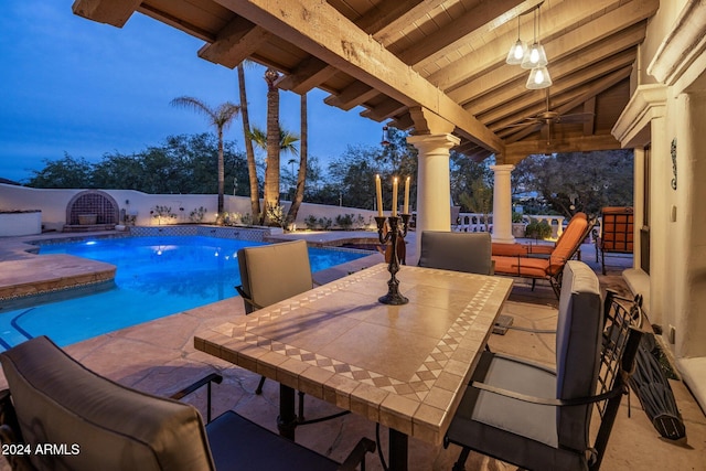 pool at dusk featuring pool water feature, ceiling fan, and a patio area