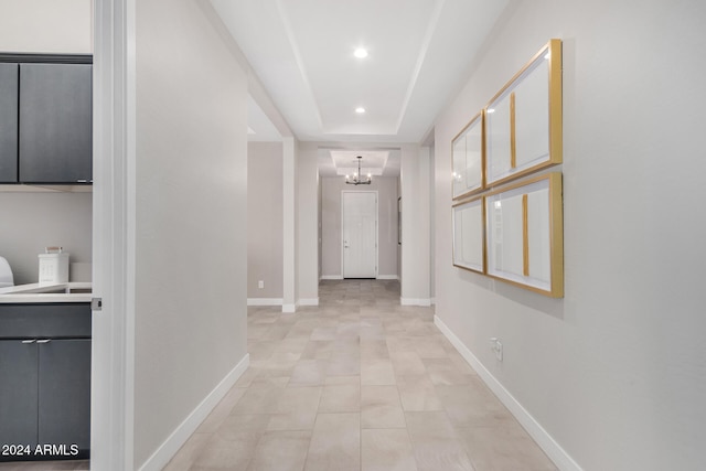 hallway featuring a tray ceiling and a notable chandelier