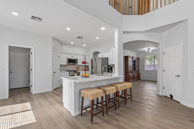 18132 W Cardinal Dr, Goodyear, AZ 85338 - kitchen featuring appliances with stainless steel finishes, arched walkways, white cabinets, light wood-style floors, and recessed lighting