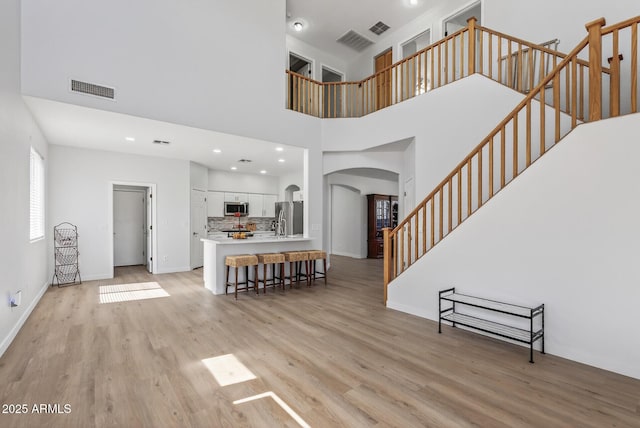 18132 W Cardinal Dr, Goodyear, AZ 85338 - living area featuring arched walkways, light wood finished floors, stairs, a high ceiling, and recessed lighting