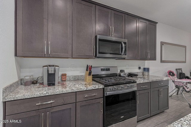 kitchen with dark brown cabinets, light stone countertops, and stainless steel appliances