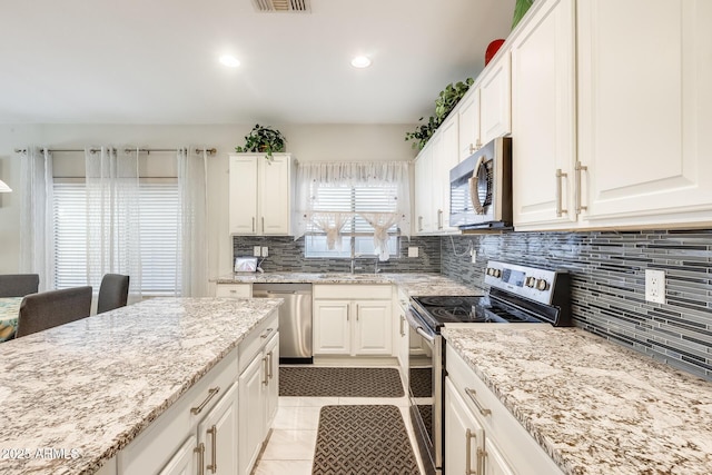 kitchen with light stone countertops, white cabinets, appliances with stainless steel finishes, sink, and light tile patterned floors