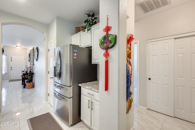 kitchen with stainless steel refrigerator with ice dispenser, white cabinetry, and light stone countertops