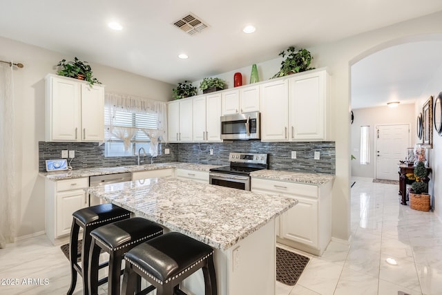 kitchen with white cabinets, appliances with stainless steel finishes, a kitchen island, sink, and light stone counters