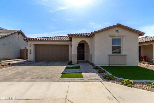 mediterranean / spanish home featuring a garage, decorative driveway, a tile roof, and stucco siding