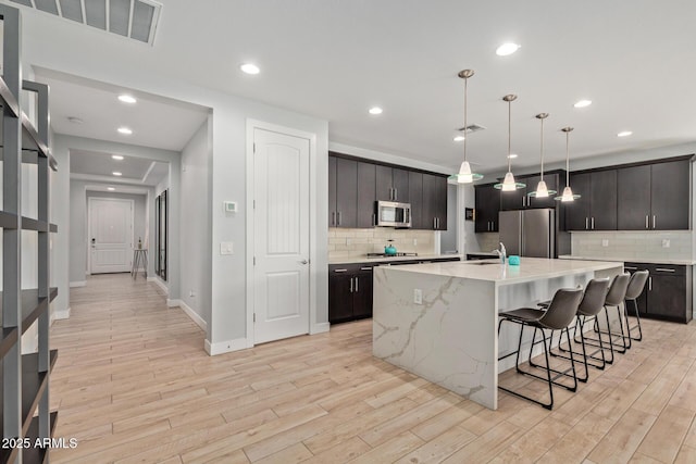 kitchen featuring appliances with stainless steel finishes, a breakfast bar, light wood-style flooring, and visible vents