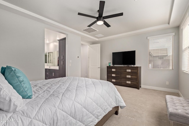 bedroom with ensuite bathroom, light colored carpet, visible vents, baseboards, and a raised ceiling