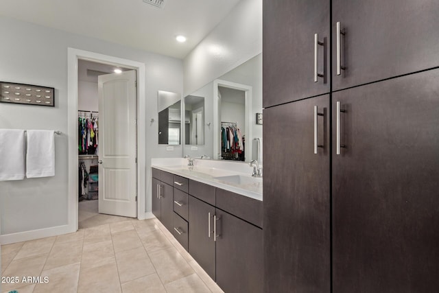 full bath featuring double vanity, a spacious closet, a sink, baseboards, and tile patterned floors