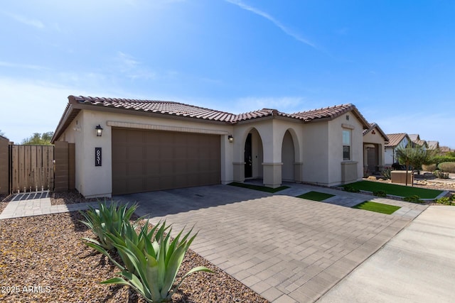 mediterranean / spanish house featuring a garage, decorative driveway, a tile roof, and stucco siding