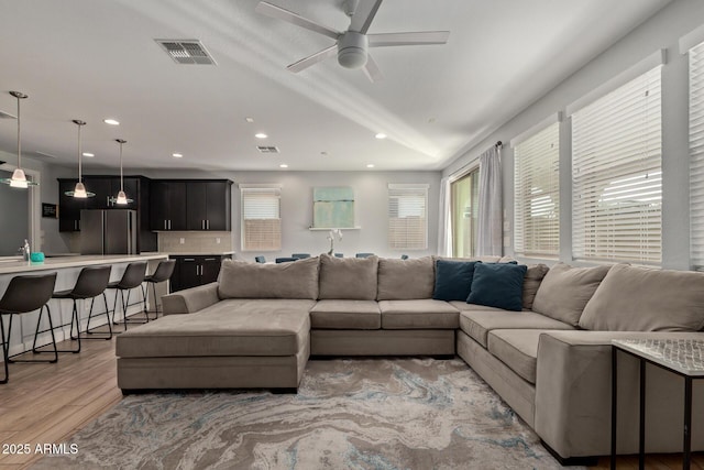 living room featuring light wood-type flooring, ceiling fan, visible vents, and recessed lighting