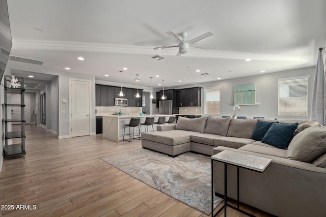 living room with light wood-style flooring, visible vents, ceiling fan, and recessed lighting