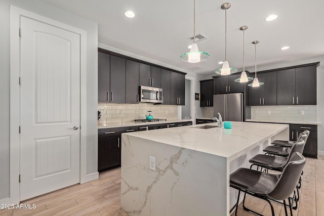 kitchen with a sink, visible vents, appliances with stainless steel finishes, a kitchen bar, and pendant lighting