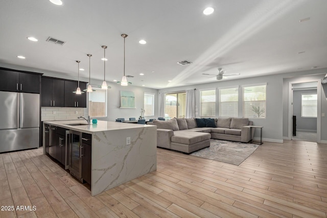 kitchen with an island with sink, visible vents, stainless steel refrigerator, and open floor plan