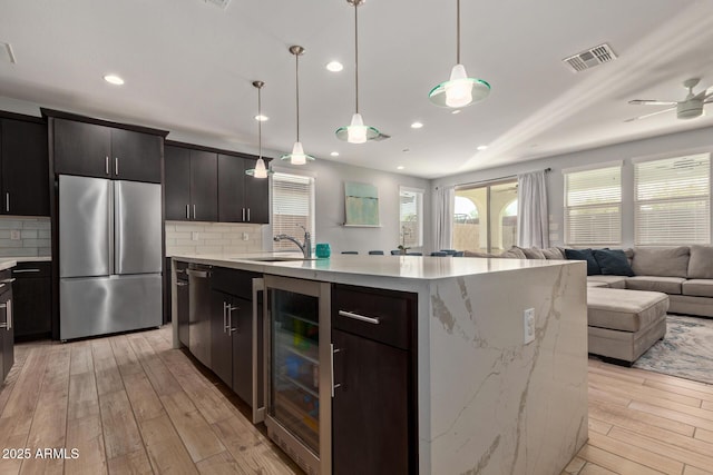 kitchen with wine cooler, visible vents, open floor plan, a sink, and stainless steel fridge