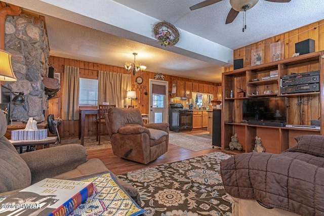 living room with wood walls, wood finished floors, and ceiling fan with notable chandelier