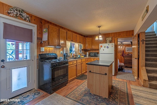kitchen featuring wood walls, a sink, freestanding refrigerator, a textured ceiling, and black gas range