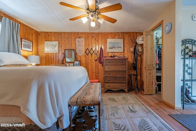 bedroom featuring baseboards, a ceiling fan, wood finished floors, and wooden walls
