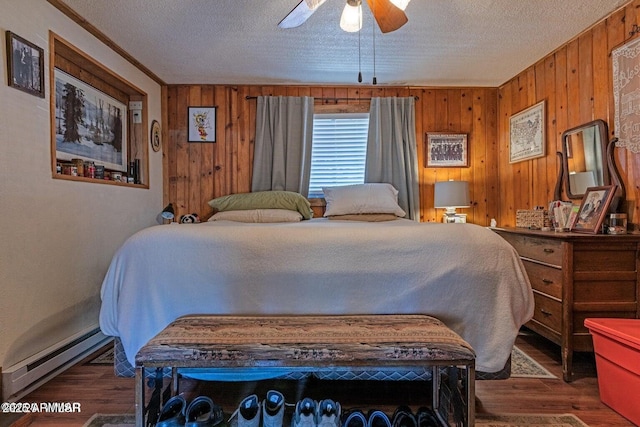 bedroom with a textured ceiling, baseboard heating, wood finished floors, ceiling fan, and wooden walls