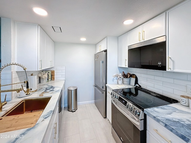 kitchen with sink, white cabinetry, stainless steel appliances, light stone counters, and decorative backsplash