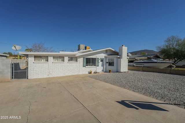 ranch-style home featuring a gate, fence, a chimney, and central AC unit