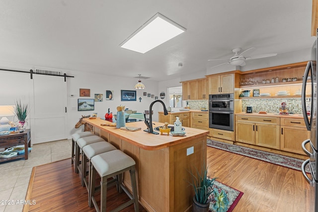 kitchen with sink, hardwood / wood-style floors, stainless steel appliances, decorative backsplash, and a barn door