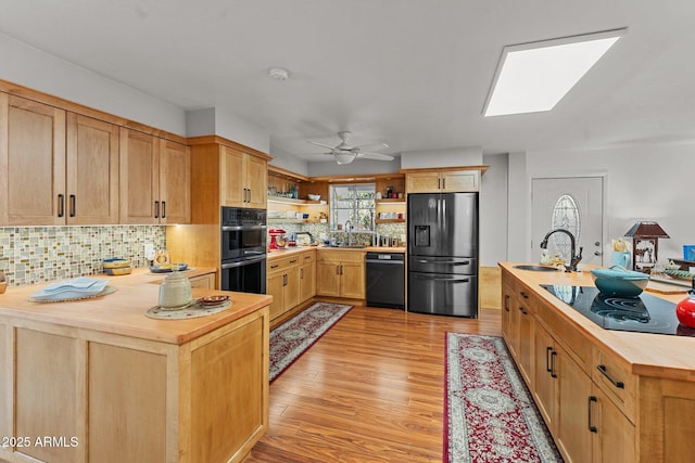 kitchen featuring butcher block countertops, tasteful backsplash, sink, light hardwood / wood-style floors, and black appliances