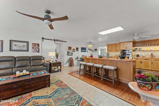 living room with ceiling fan, a barn door, and light tile patterned floors