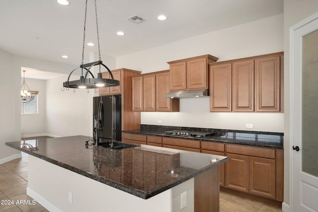 kitchen with hanging light fixtures, light tile patterned flooring, black appliances, and a center island with sink