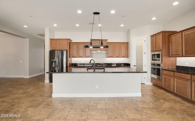 kitchen with sink, appliances with stainless steel finishes, hanging light fixtures, a center island with sink, and dark stone counters