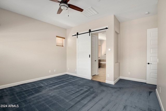 unfurnished bedroom featuring ceiling fan, a barn door, carpet flooring, and ensuite bath