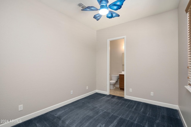 unfurnished bedroom featuring ceiling fan, dark carpet, and ensuite bath