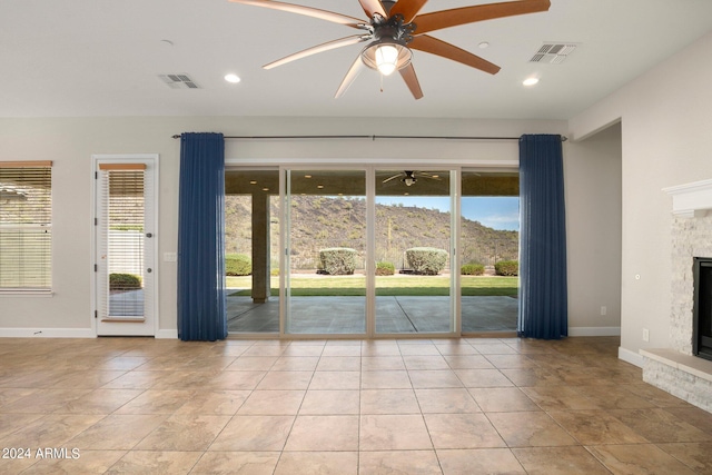 unfurnished living room featuring ceiling fan, a stone fireplace, a healthy amount of sunlight, and a mountain view