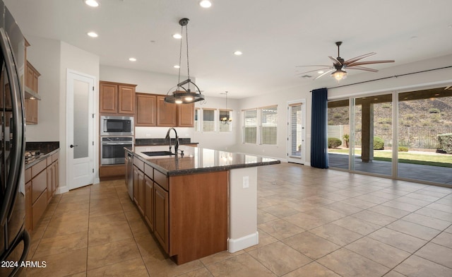 kitchen with appliances with stainless steel finishes, pendant lighting, an island with sink, sink, and dark stone counters