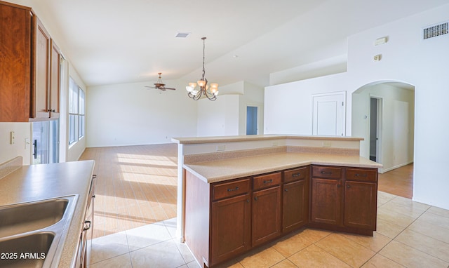 kitchen with ceiling fan with notable chandelier, vaulted ceiling, pendant lighting, light tile patterned floors, and a kitchen island