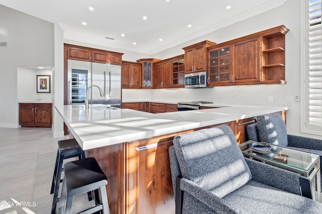 kitchen with kitchen peninsula, stainless steel appliances, ornamental molding, light tile patterned flooring, and a kitchen bar