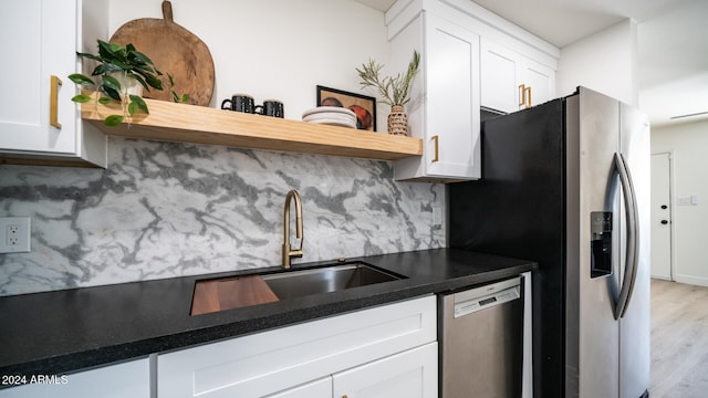 kitchen with appliances with stainless steel finishes, sink, light hardwood / wood-style floors, white cabinets, and decorative backsplash