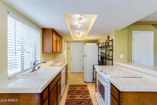 kitchen featuring white appliances, sink, light tile patterned floors, tile counters, and kitchen peninsula