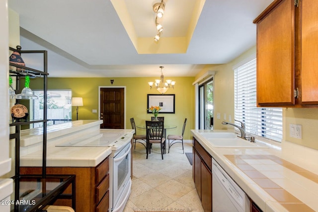 kitchen with white appliances, a tray ceiling, sink, tile countertops, and a chandelier