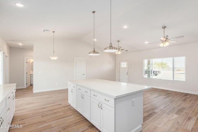 kitchen with light stone countertops, a kitchen island, white cabinetry, and pendant lighting