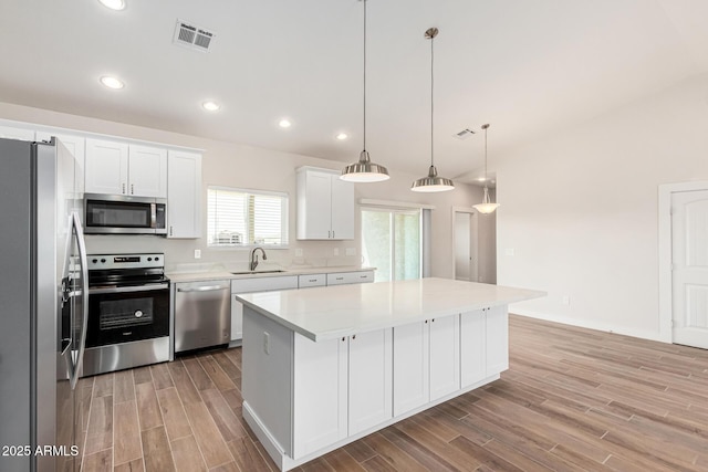 kitchen featuring decorative light fixtures, white cabinetry, appliances with stainless steel finishes, and a kitchen island