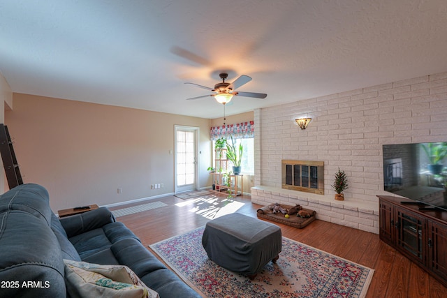 living room featuring a brick fireplace, wood-type flooring, a textured ceiling, and ceiling fan