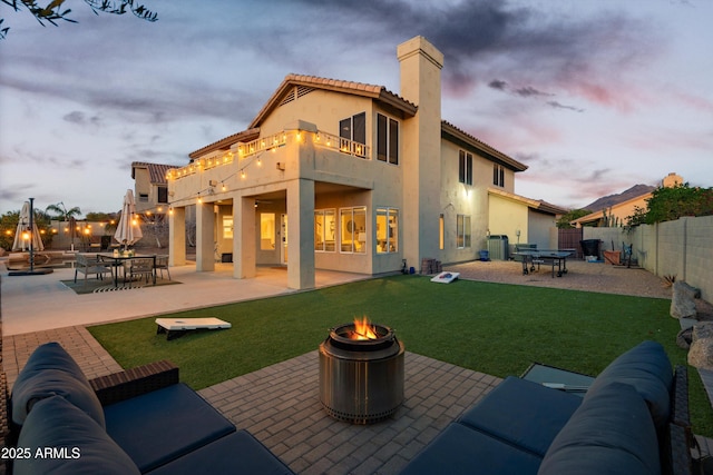 back of property at dusk with a balcony, a patio area, an outdoor fire pit, and central AC